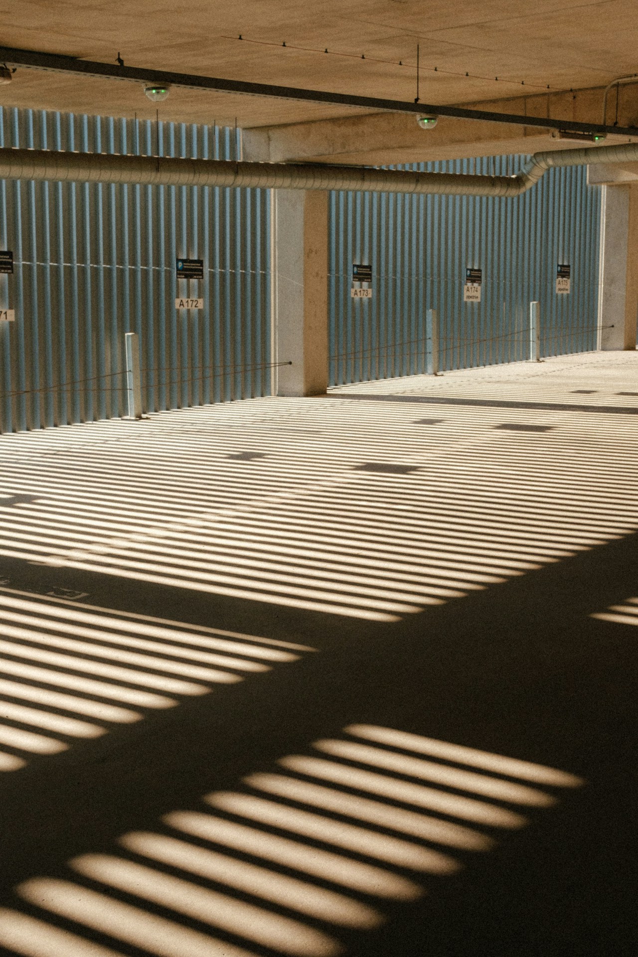 Places de parking couvertes vides, lumière naturelle. Aucune voiture, aucune plaque, aucune personne. Les panneaux portent les numéros des places. — Genet Schneider · Unsplash License. Crédits : mystaylink.com/storage/jade-credits.html